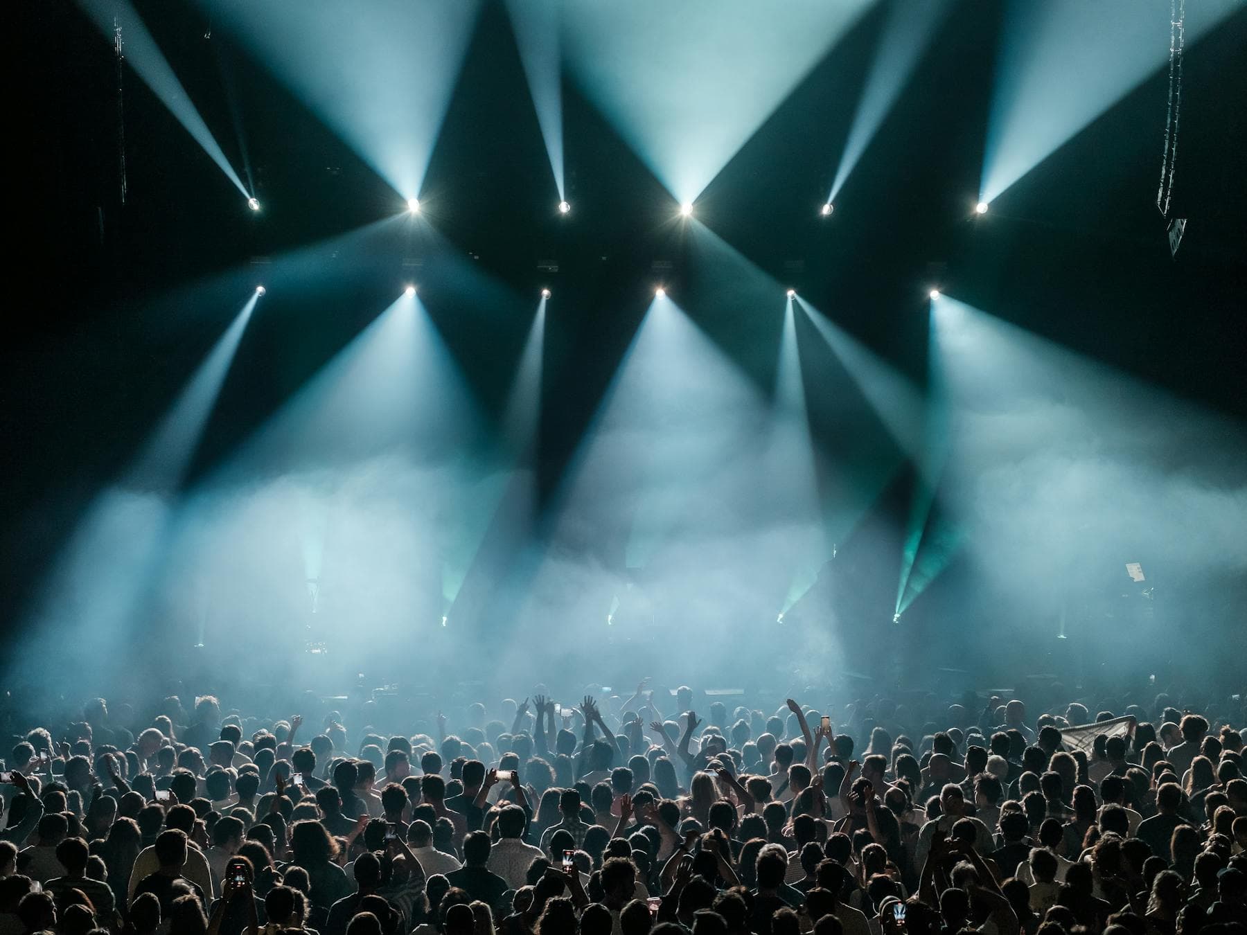 Stage beam lights cutting through fog above a packed concert crowd